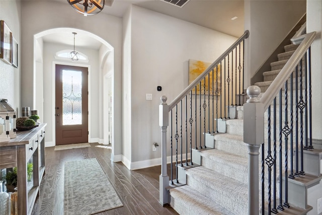 entrance foyer featuring baseboards, visible vents, arched walkways, and dark wood-type flooring