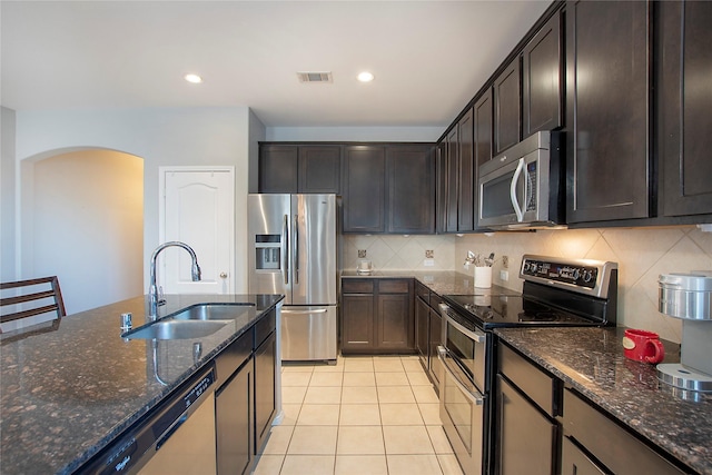 kitchen with visible vents, dark stone counters, appliances with stainless steel finishes, dark brown cabinets, and a sink