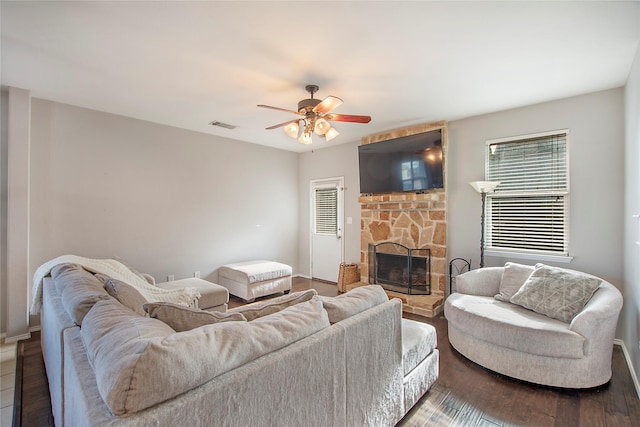 living room with ceiling fan, visible vents, wood finished floors, and a stone fireplace