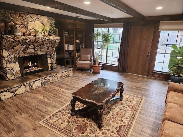 living room featuring beam ceiling, a healthy amount of sunlight, a stone fireplace, and hardwood / wood-style flooring