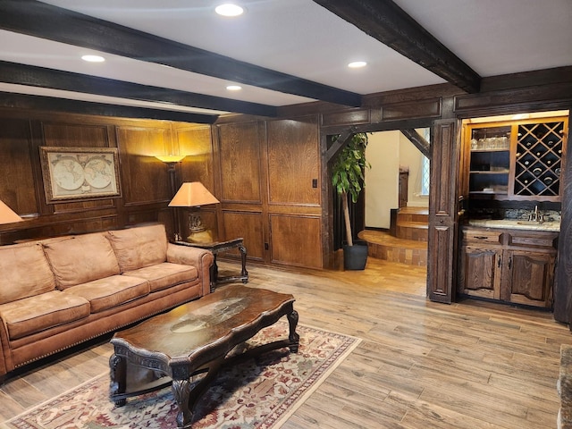 living area with wood walls, light wood-style flooring, bar area, and beam ceiling