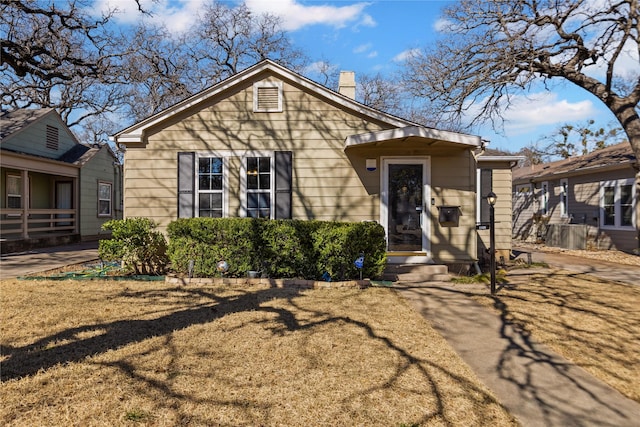 bungalow-style home featuring entry steps, a chimney, and a front lawn