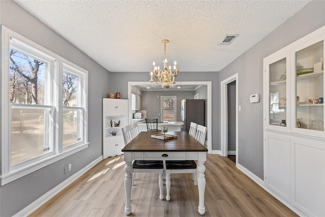 dining room featuring a chandelier, visible vents, light wood-style flooring, and a textured ceiling