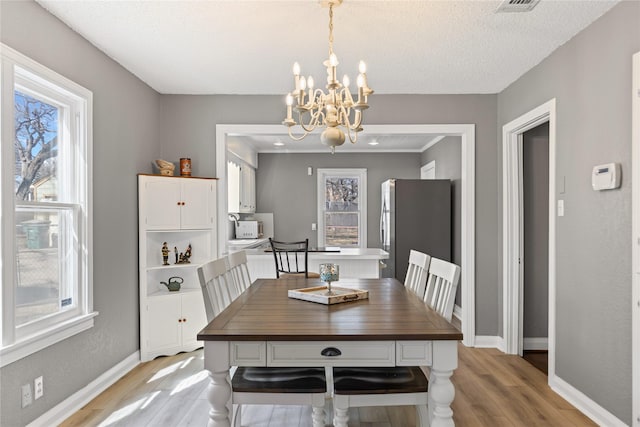 dining room featuring an inviting chandelier, light wood-style flooring, baseboards, and a textured ceiling