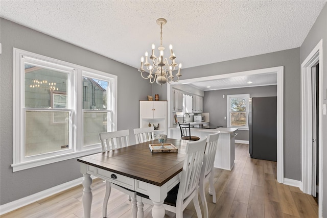 dining area with light wood-style floors, a notable chandelier, baseboards, and a textured ceiling