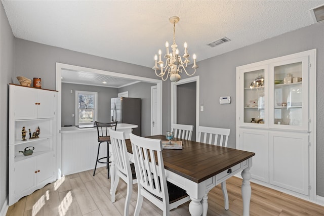 dining room with a wainscoted wall, visible vents, light wood-style flooring, an inviting chandelier, and a textured ceiling