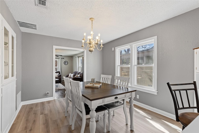 dining room featuring baseboards, light wood-style flooring, visible vents, and a notable chandelier