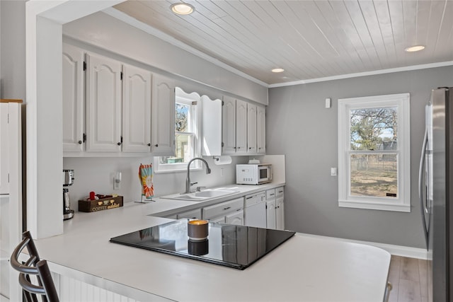 kitchen featuring white microwave, a sink, white cabinetry, light countertops, and freestanding refrigerator