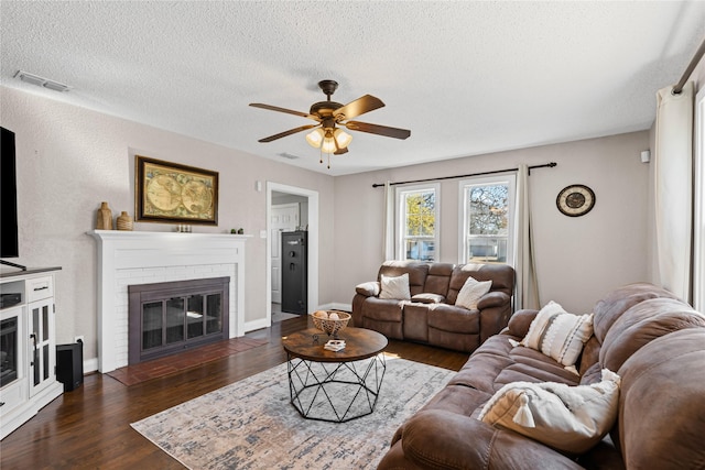 living room featuring ceiling fan, a fireplace, dark wood finished floors, and visible vents