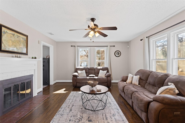 living area with a brick fireplace, visible vents, dark wood finished floors, and a textured ceiling