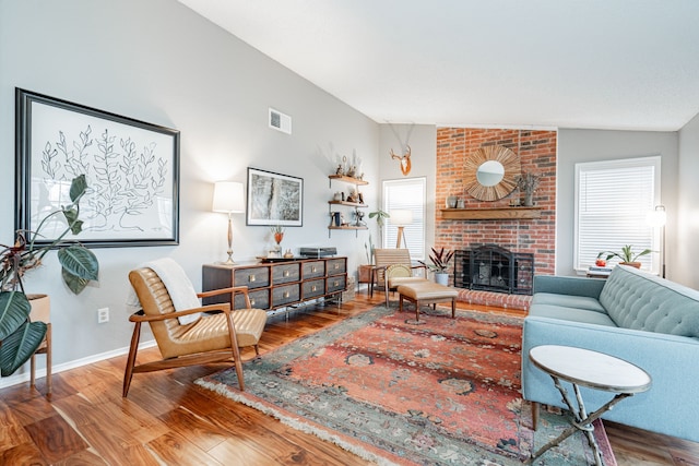 living area featuring baseboards, visible vents, wood finished floors, vaulted ceiling, and a brick fireplace