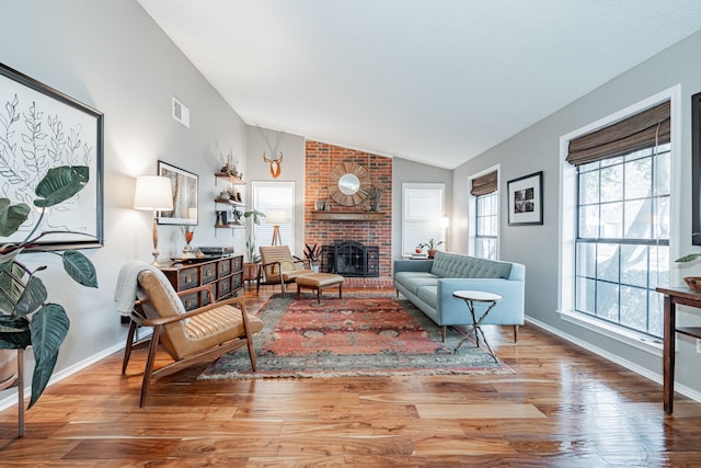 living area featuring visible vents, a brick fireplace, vaulted ceiling, wood finished floors, and baseboards