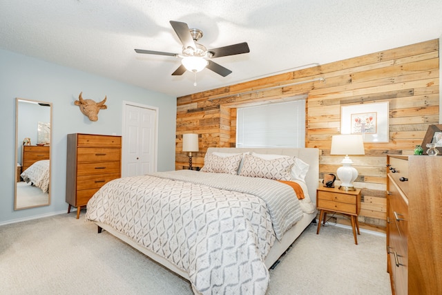 bedroom with wooden walls, light colored carpet, ceiling fan, a textured ceiling, and a closet