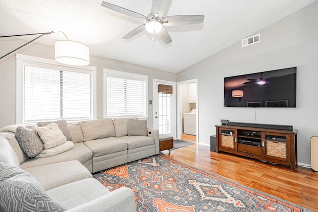 living area featuring visible vents, vaulted ceiling, wood finished floors, washer / dryer, and plenty of natural light