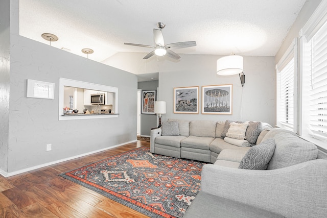 living area with dark wood-style floors, a ceiling fan, vaulted ceiling, a textured ceiling, and baseboards