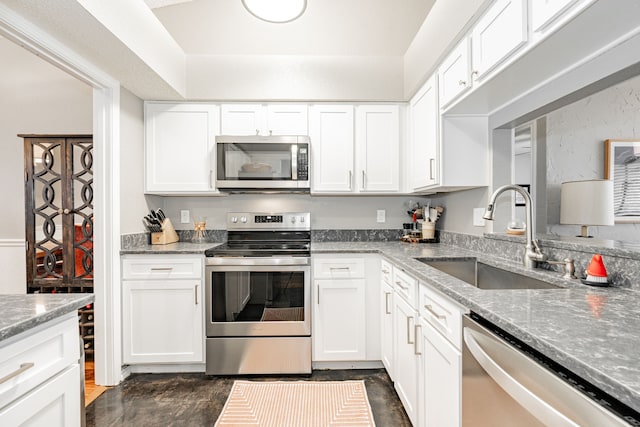 kitchen with light stone counters, appliances with stainless steel finishes, white cabinets, and a sink