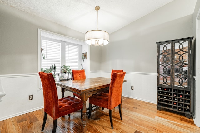 dining room featuring a textured ceiling, wainscoting, a chandelier, and light wood-style floors