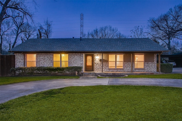 ranch-style home featuring driveway, stone siding, a shingled roof, and a front lawn