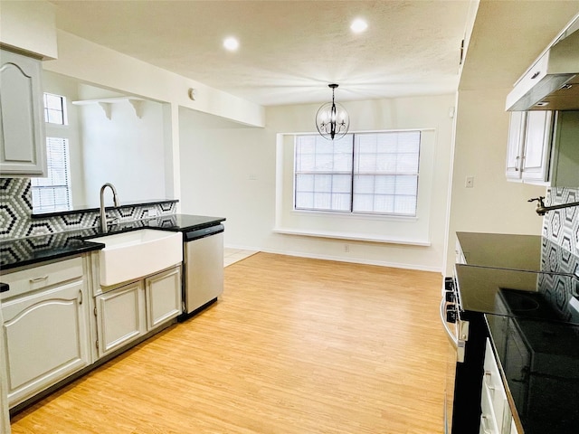 kitchen with under cabinet range hood, a sink, hanging light fixtures, dishwasher, and dark countertops