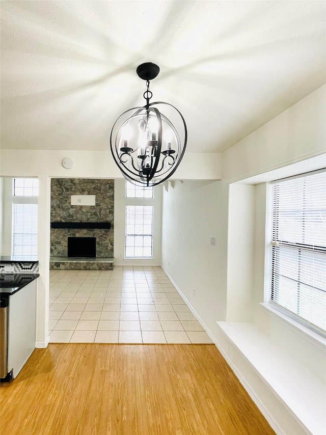 unfurnished dining area featuring a healthy amount of sunlight, a chandelier, and a stone fireplace