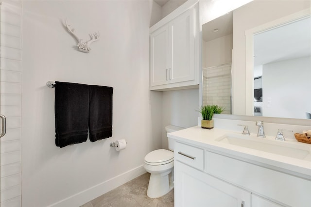 bathroom with toilet, a stall shower, baseboards, and vanity