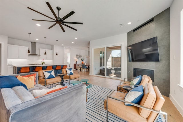 living room with recessed lighting, visible vents, a ceiling fan, light wood finished floors, and a tiled fireplace