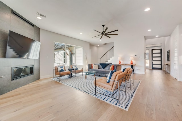 living area featuring recessed lighting, visible vents, light wood-style flooring, a tile fireplace, and stairs