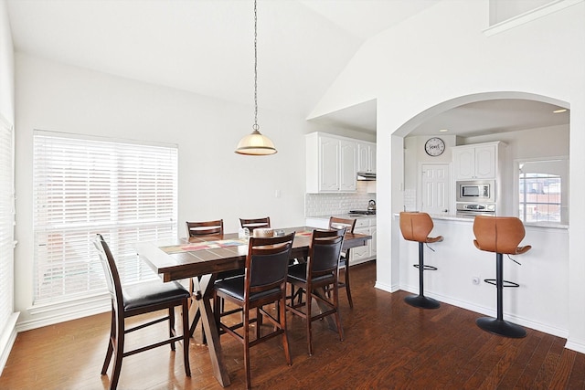 dining area with arched walkways, high vaulted ceiling, dark wood-type flooring, and baseboards