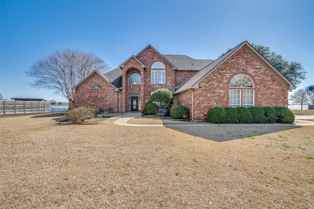 traditional home with a front yard, fence, and brick siding