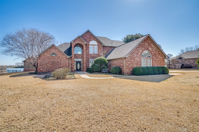 traditional-style house with brick siding, a front lawn, a shingled roof, and fence