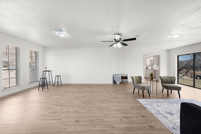 living area featuring a textured ceiling, ceiling fan, visible vents, and light wood-style floors