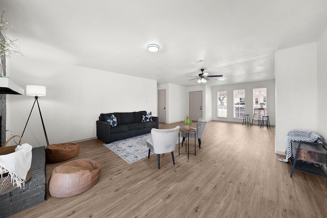 living area featuring ceiling fan, light wood-type flooring, visible vents, and a brick fireplace