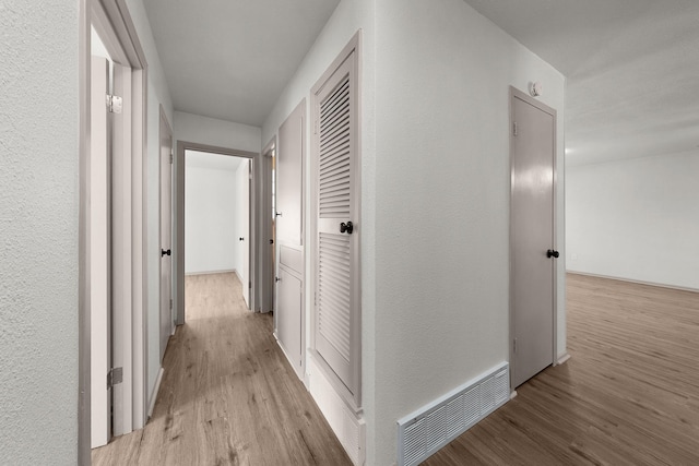 hallway featuring visible vents, a textured wall, and light wood-style flooring