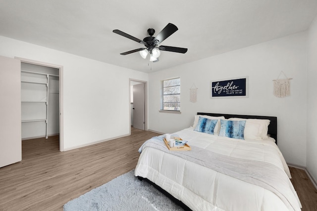 bedroom with ceiling fan, a spacious closet, baseboards, and wood finished floors