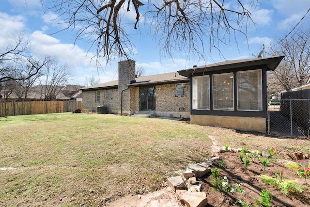 back of house featuring a sunroom, a chimney, fence, and a lawn