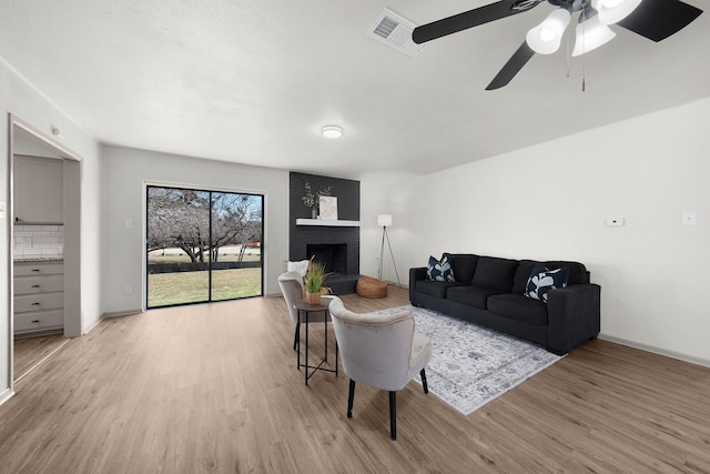 living area featuring light wood-style flooring, a brick fireplace, visible vents, and baseboards