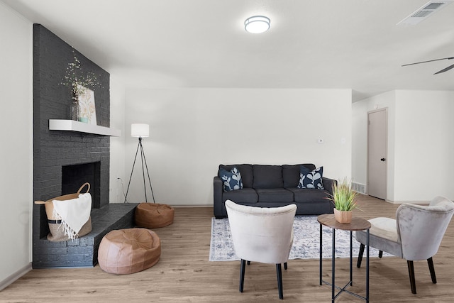 living room with a fireplace, visible vents, a ceiling fan, wood finished floors, and baseboards