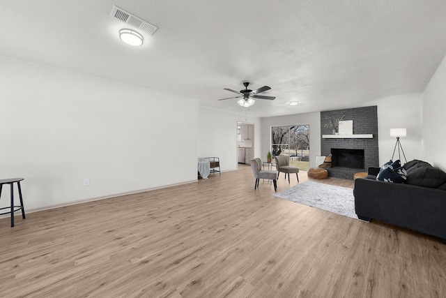 living room featuring a fireplace, light wood finished floors, visible vents, a ceiling fan, and a textured ceiling