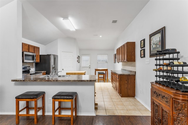 kitchen with visible vents, dark countertops, a peninsula, vaulted ceiling, and stainless steel appliances