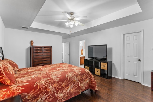 bedroom featuring a tray ceiling, dark wood-style flooring, visible vents, ensuite bathroom, and baseboards