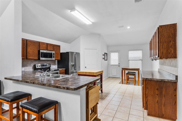 kitchen with light tile patterned floors, stainless steel appliances, lofted ceiling, decorative backsplash, and a peninsula