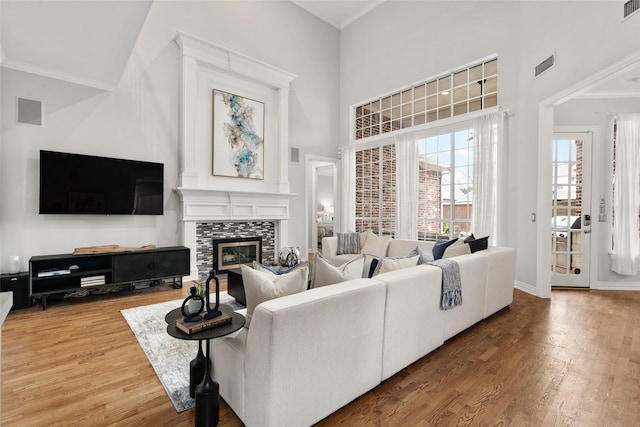 living room featuring visible vents, a tile fireplace, wood finished floors, and a towering ceiling