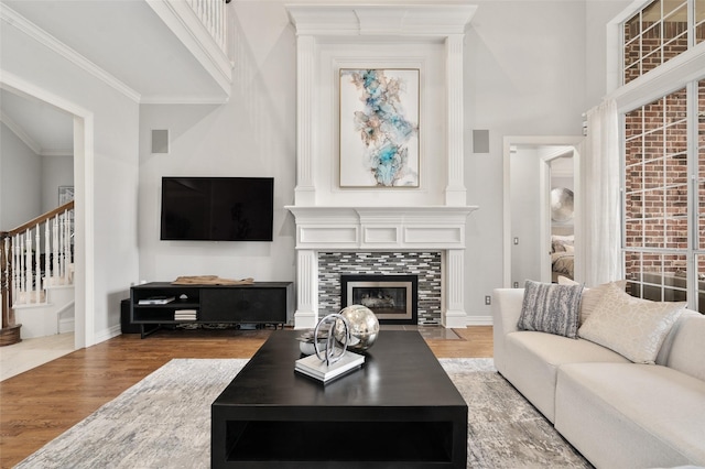 living room with a tiled fireplace, wood finished floors, a towering ceiling, and crown molding