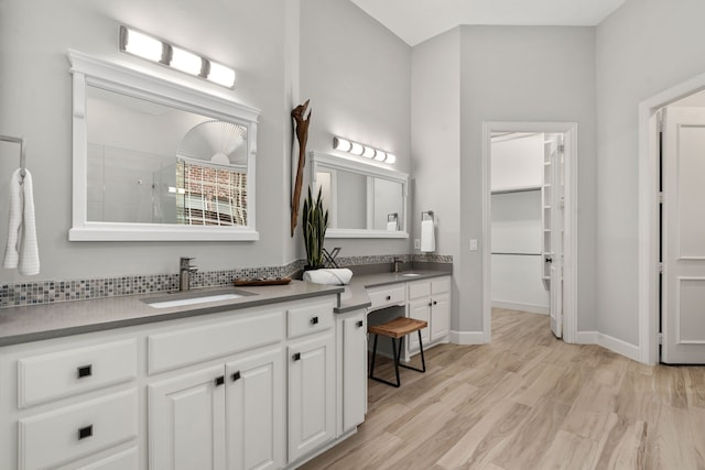 bathroom featuring wood finished floors, vanity, baseboards, a tile shower, and a walk in closet