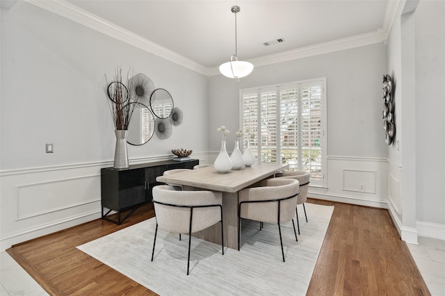 dining room featuring wainscoting, visible vents, light wood finished floors, and ornamental molding