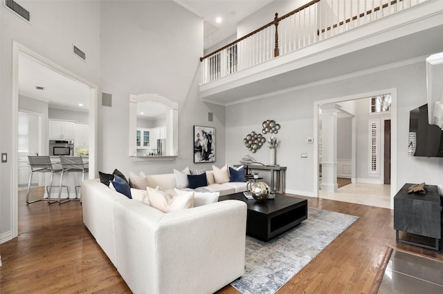 living area with decorative columns, a high ceiling, visible vents, and wood finished floors