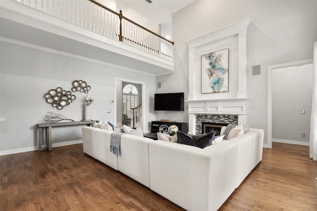 living room featuring a high ceiling, a tiled fireplace, wood finished floors, and baseboards