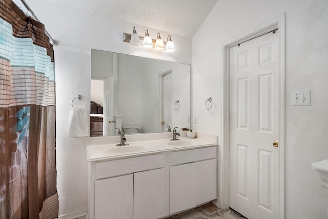 bathroom featuring a sink, a textured ceiling, toilet, and double vanity