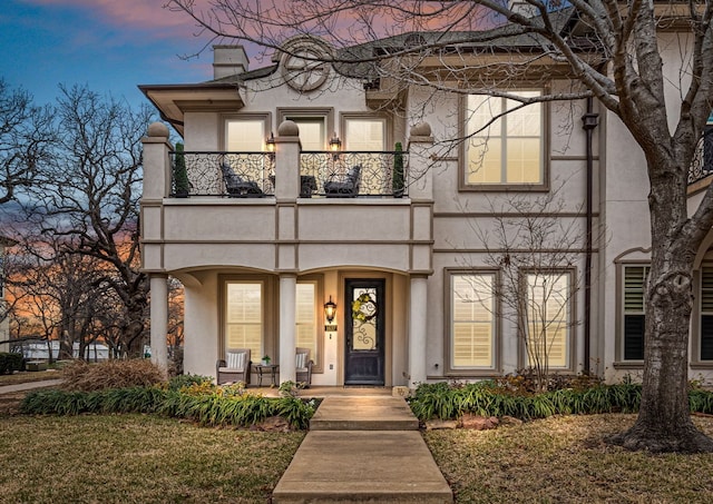 view of front of property with a chimney, a balcony, and stucco siding