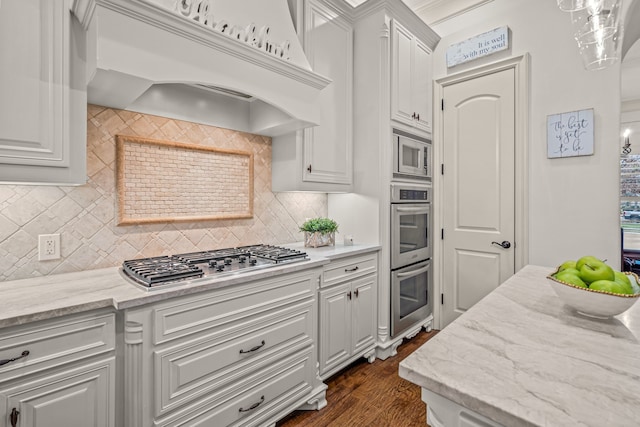 kitchen with stainless steel appliances, light stone countertops, white cabinetry, and custom range hood